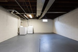 Washer and dryer side-by-side in an empty, large basement.